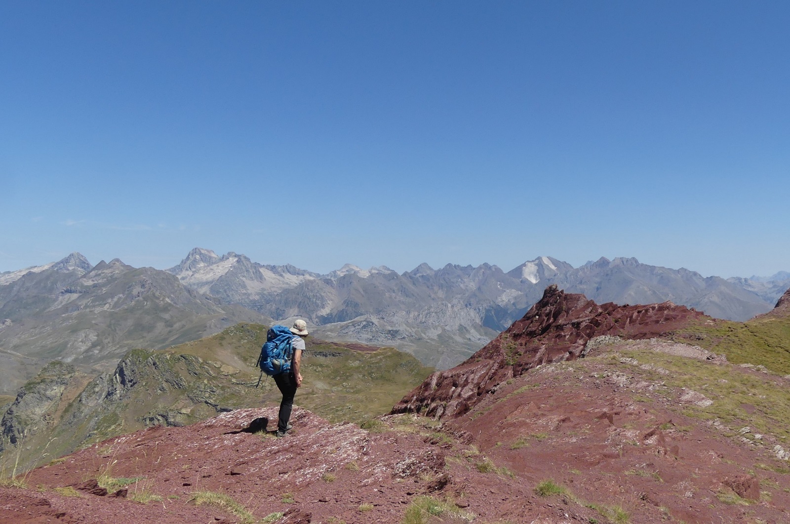 Photo de Christelle sur une crête rouge foncé ; on voit une chaîne de montagnes derrière elle.